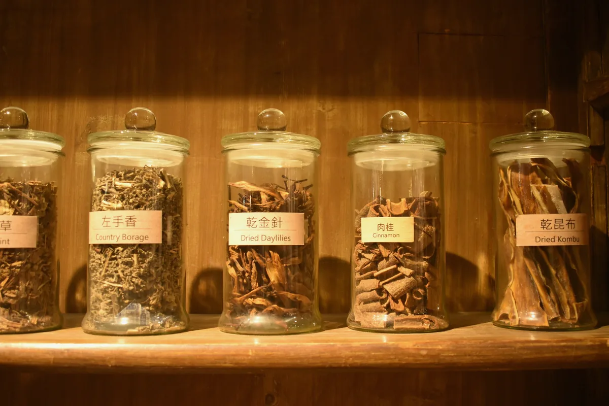 Rangée de bocaux en verre remplis de racines et d'herbes séchées sur une étagère en bois