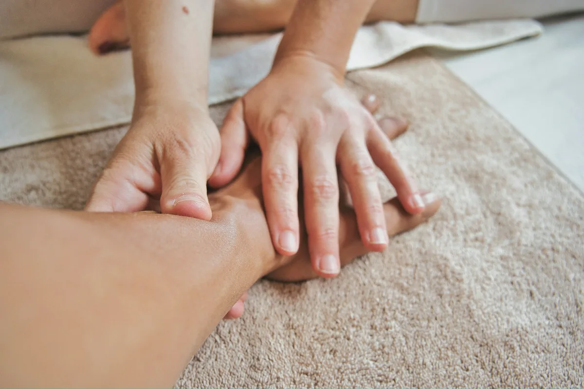 Mains posées à plat sur un bras, sur un tissu beige, dans un geste de massage