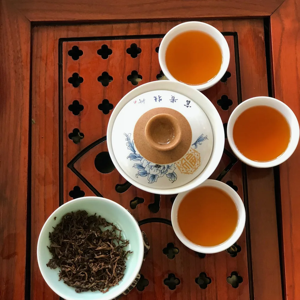Plateau à thé en bois ajouré vu de dessus, avec un gaiwan et quatre tasses de thé ambré