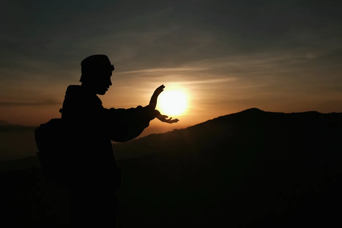 Silhouette en contre-jour face au soleil levant, une main ouverte, dans un mouvement de qi gong